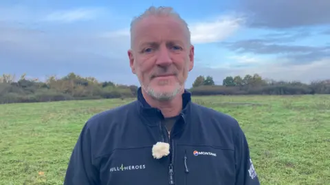 Jo Makel/BBC Head and shoulders shot of Paul Matson. He is standing on a field and is wearing a black jacket with the Hull4Heroes emblem on it.