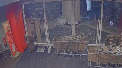 Devon and Cornwall Police Crimp is seen throwing a brick at the glass door of TK Maxx and the glass cracks from the impact