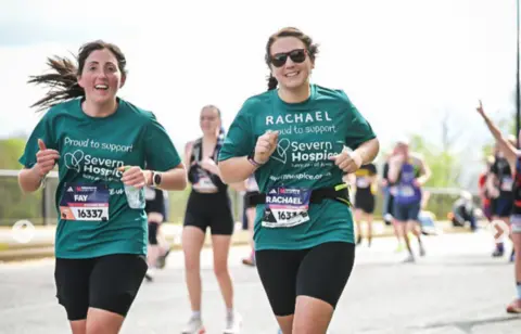 Rachael Ganderton Two women with long brown hair and green tops running, with one of them wearing sunglasses and a number of other runners in the background