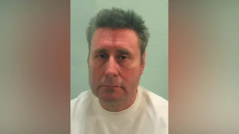 A mugshot image of a middle-aged male prisoner wearing a white top. 