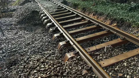 A picture of a railway track where the ballast have been washed away and moved following storm damage. 