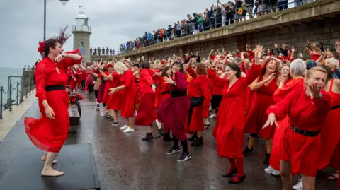 Andrew Aitchison/Getty Images Hundreds of Kate Bush fans came together today wearing red floaty dresses on Folkestone's Harbour Arm to dance to her most iconic song, Wuthering Heights on the 20th of July 2025 in Folkestone, United Kingdom. 
