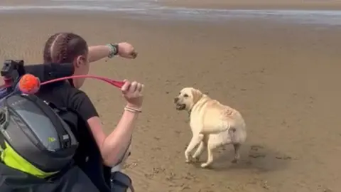 RNLI Jo Jones throws a ball to her dog Yoda on the beach.