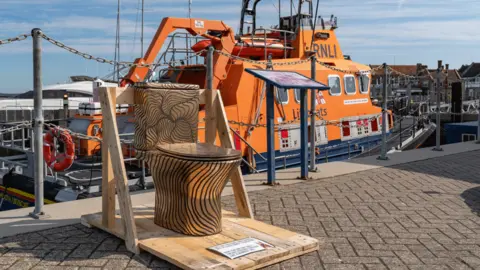 Sienna Anderson A gold striped toilet at a port, an RNLI boat behind it.