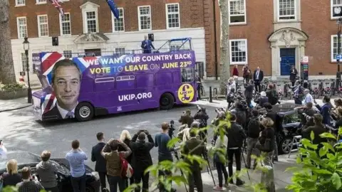 Getty Images A double decker bus coloured purple with a large picture of Nigel Farage's face on the side, with the slogan "We want our country back - vote to leave on June 23rd". It is driving past a crowd of people, mainly photographers, in a London street which has three-storey brick buildings on the opposite side of the road.