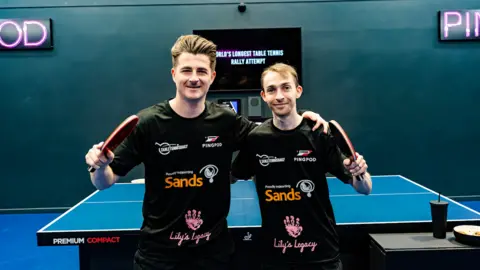 Tom Lewis Image of Dan Ives and Lloyd Gregory. They are by a table tennis table. 