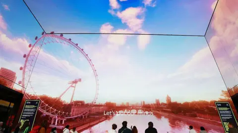 Getty Images People viewed from behind looking at an immersive, floor-to-ceiling wraparound digital screen displaying an image of the London Eye and the River Thames.