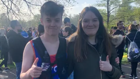 Darren Nunn Billy Nunn and his sister give a thumbs up to the camera. Billy is a young man wearing a running vest. His sister has long dark hair and is wearing a coat with a fur-trimmed hood.