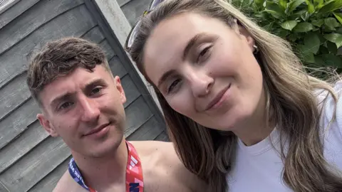 Will Rotheram A selfie of Will and Laura after Will ran the Manchester half-marathon. He has short brown hair and is wearing a medal around his neck. Laura has long brown hair, is wearing a white top, and glasses upon her head.