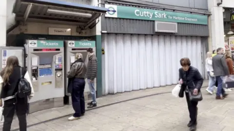 BBC Exterior of Cutty Sark station with shutters pulled across and members of the public walking past