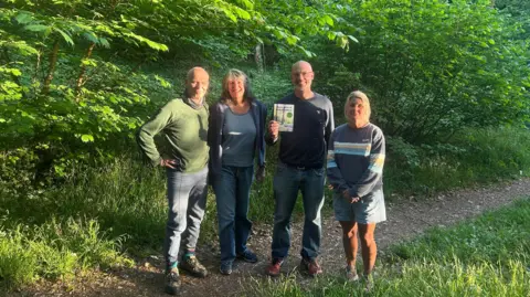 A group of people, two men and two women standing in woodland. 