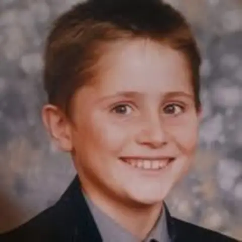 Family handout A school portrait of a boy around 12 years old in a black blazer and grey shirt. He has brown eyes and brown hair.
