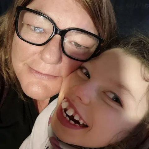 Patricia Risbridger Selfie of Patricia Risbridger and Esmai. Patricia has black-rimmed glasses. Esmai has a wide beaming smile.