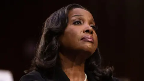Getty Images Lisa Cook, a black woman with shoulder-length hair, stares into the middle distance. She is wearing a black coat and a string of white pearls.
