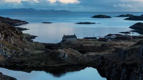 John Maher A view across a landscape of lochs and rocky coast, dotted by a few houses in Bays of Harris in the Western Isles.