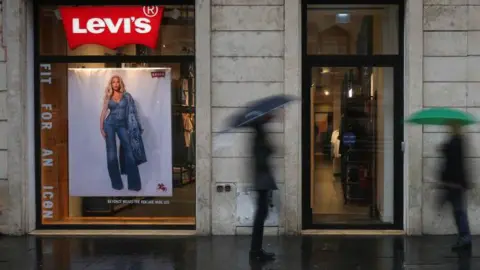 Getty Images two men with umbrellas, unclear in the picture, walking next to a store that sells jeans