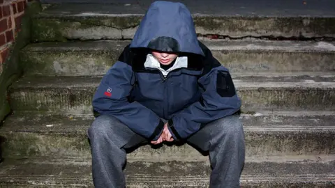 Generic image of an unidentified teenager sitting on stone steps with his hood up