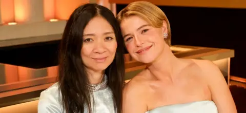 Getty Images Chloé Zhao and Jessie Buckley attend the 83rd Annual Golden Globe Awards at The Beverly Hilton on January 11, 2026 in Beverly Hills, California. The pair are both dressed in silver and are smiling at the camera.