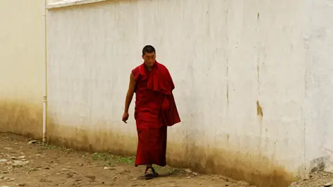 Xiqing Wang/ BBC A monk walking down a street 
