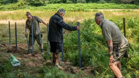 Andres Jablonski Three men in countryside location, holding posts in the ground