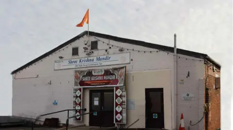 Dharam Awesti A white building with a black roof and red and orange flying from the top.