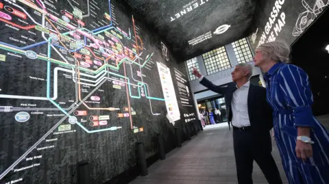 PA Media The mayor points to an illuminated music Tube map onh a wall.