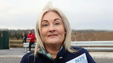 PA Media Verona Murphy wearing her blonde hair down with a navy coat on standing in front of a coast line 