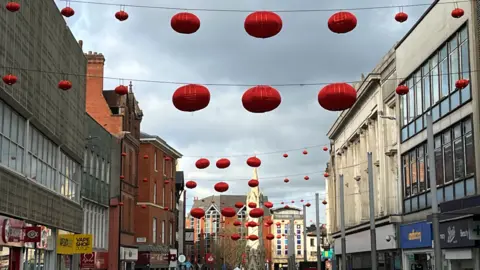 Linternas chinas rojas de la BBC que cuelgan de un edificio a otro en el centro de la ciudad de Leicester cerca de la torre del reloj