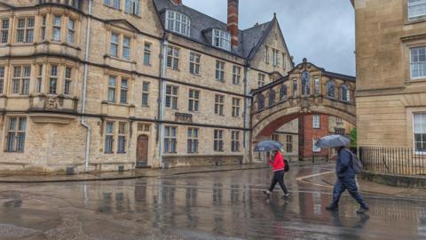 FRIDAY - Two people walk past the Bridge of Sighs in Oxford with umbrellas in the rain