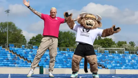 Iwan Thomas and Bab, the official mascot for the championships, jumping in the air in an empty stadium.
