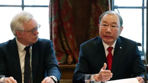 EPA Conservative MP David Davis and Professor Dr Shoo Lee sit side-by-side at a press conference to unveil new evidence on the Lucy Letby case. They are both older men, wearing dark suits. The MP is wearing a dark tie, Dr Lee is wearing a red tie and has papers and a glass of water in front of him.