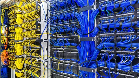 A rack with generic yellow and blue cables, part of a large company data centre.