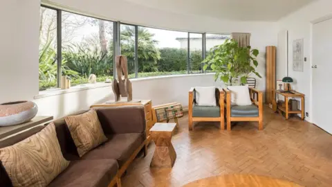 Historic England A large curved window dominates the white-pained interior, which has a herringbone wooden floor and a wooden-framed sofa, chairs and tables.