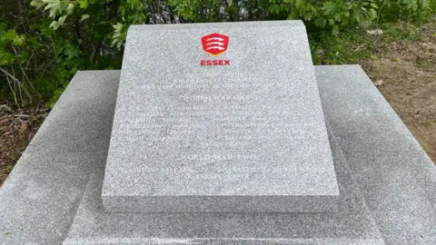 Victoria Polley/BBC A grey stone war memorial. It is a low-lying tier of three stone slabs. The top smallest slap has the names of 16 men on it.