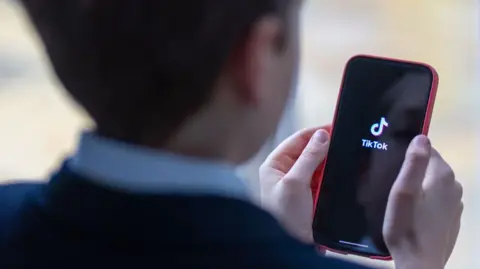 A 12-year-old school boy looks at a iPhone screen showing the social media app TikTok.