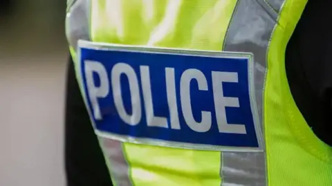 The back a high-vis police jacket with the word POLCIE written in white on a dark blue background