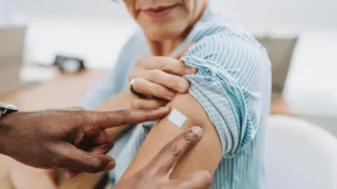 A doctor puts a plaster over a patients arm after she has had a vaccination