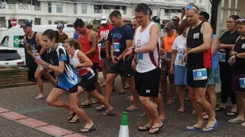 Sussex Trail Events Dozens of runners wearing flip-flops at the start of a 5k on Worthing seafront.