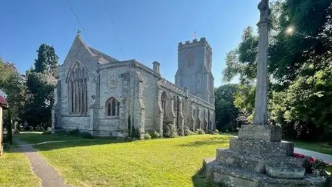 Google The exterior of St Peter & All Hallows' Church. It is a sunny day and the grass is green and cut.
