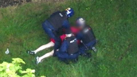 A man in a dressing gown is pinned down and arrested by police officers