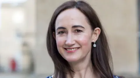 Getty Images Sophie Kinsella pictured smiling at the camera. Her long brown her has been styled down in this image. 
