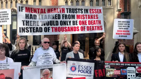 Richard Daniel/BBC Family members stand outside Arundel House in London protesting. They are holding up banners. One reads: 'Our loved ones cannot rest in peace until the truth about Essex mental health failings are exposed'.