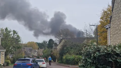 A big plume of thick black smoke can be scene in the skyline of a residential neighbourhood.