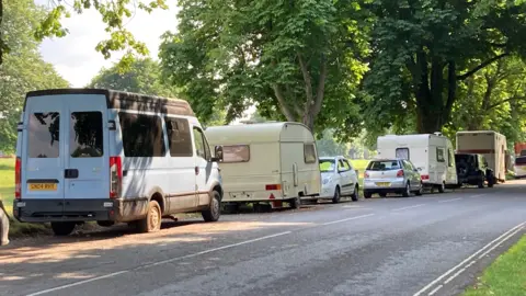 Several vehicles, including cars and campervans, parked on a road along the Clifton Downs in Bristol.