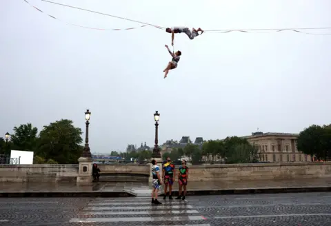   Maddie Meyer/Getty Images  Tightrope walker Nathan Paulin performs on a high rope during the athletes’ parade on the River Seine near the Supreme Court during the opening ceremony of the Olympic Games Paris 2024