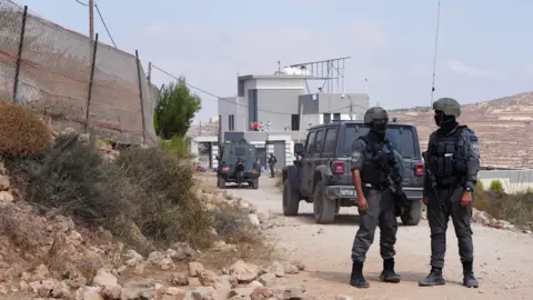 Members of the Israeli security forces stand guard near a Palestinian house, which was besieged by Israeli settlers, in Qusra