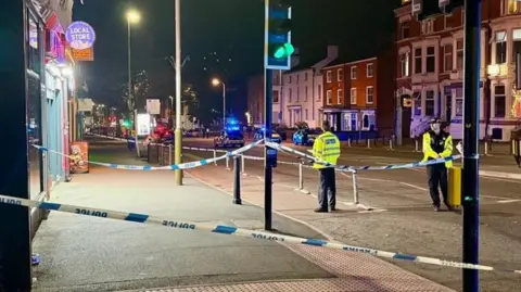 Police tape across traffic lights with two police officers in the picture.