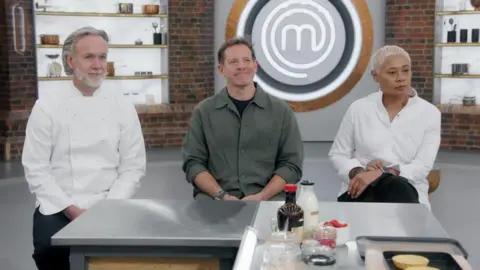 Left to right - MasterChef judges Marcus Wareing, Matt Tebbutt and Monica Galetti sitting in a studio during an episode of the show. All are looking away from the camera.