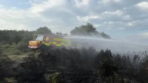 A fire engine spraying burning heathland with water