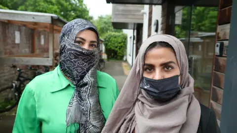 Malika wearing a green shirt and headscarf is standing next to Bella who is wearing a headscarf and face mask